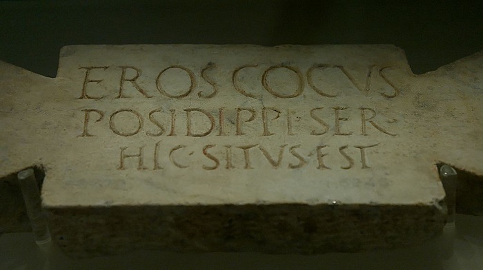 Muistokirjoitus kivilaatassa: Tässä lepää Eros, Posidippuksen kokki ja orja. 
